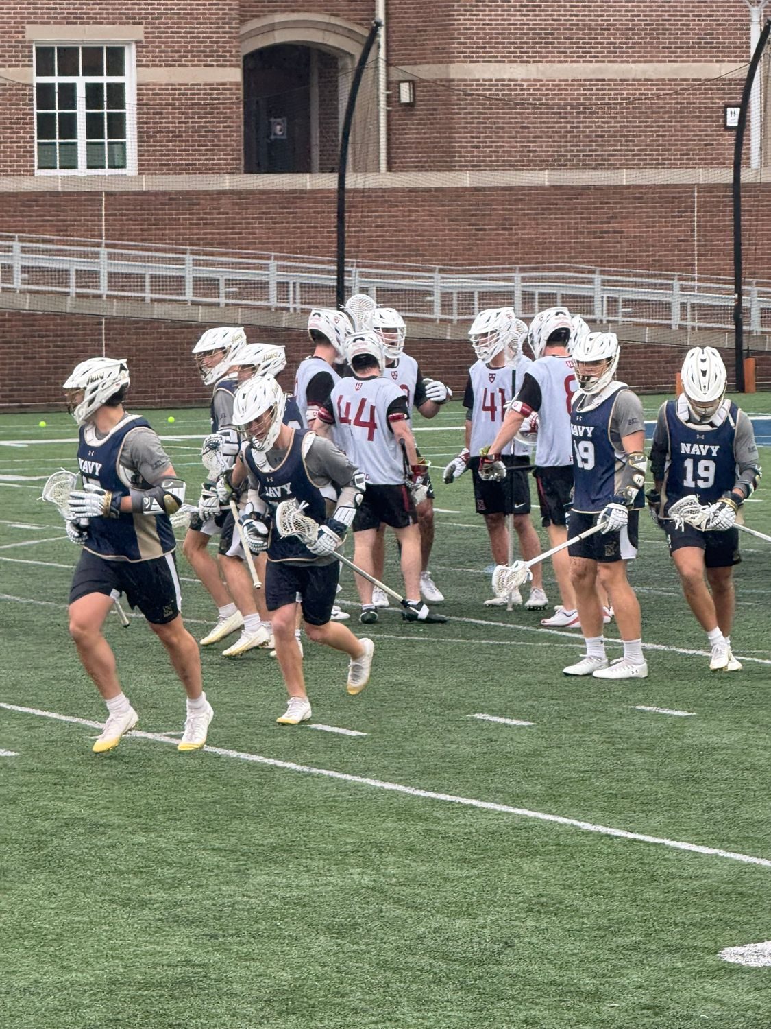 Navy and Harvard lacrosse players warming up on the field